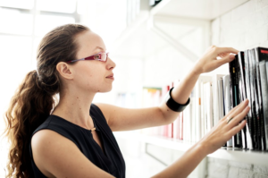 woman with glasses finding book on bookshelves