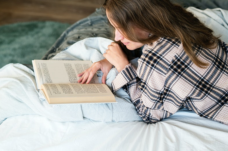 woman in plaid longsleeves reading book on bed